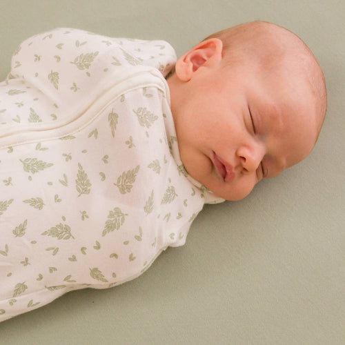Newborn baby swaddled in a light-colored blanket with a subtle pattern on a plain background
