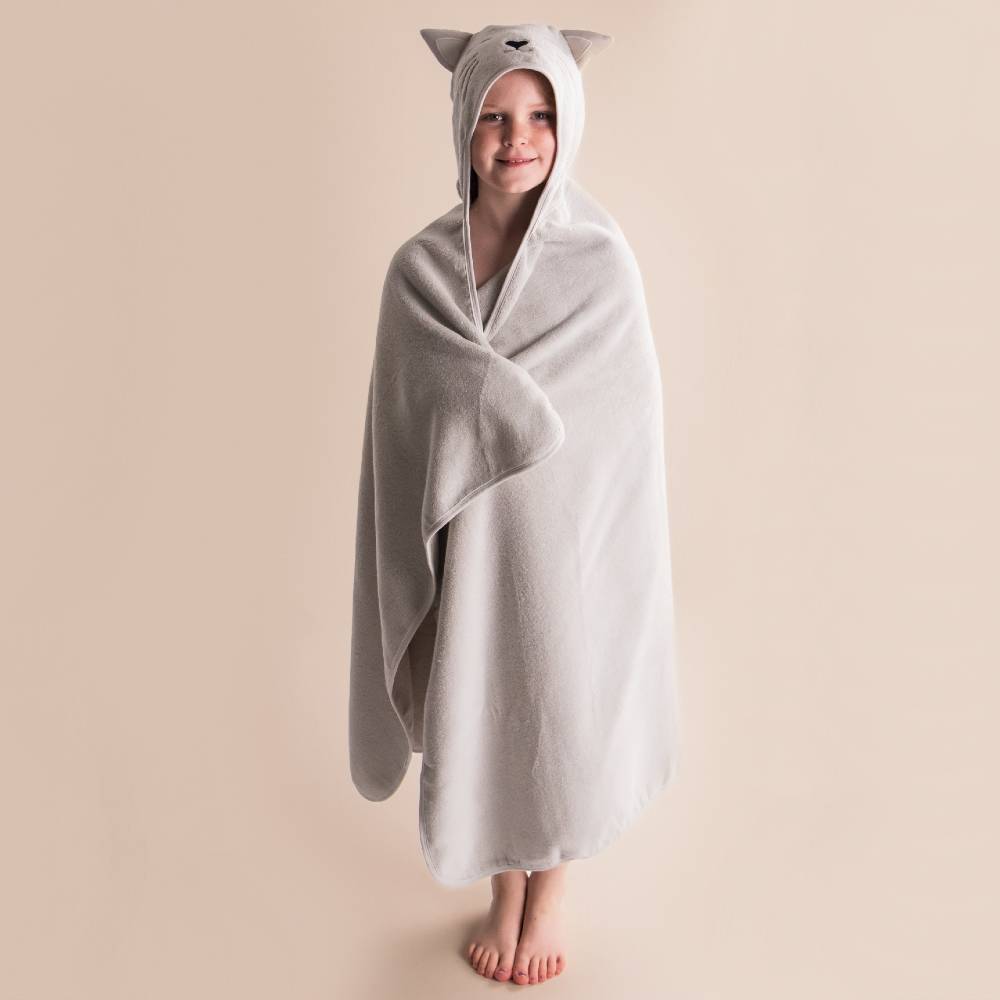 A child wrapped in a light gray hooded towel with cat-ear details, standing against a plain beige background.