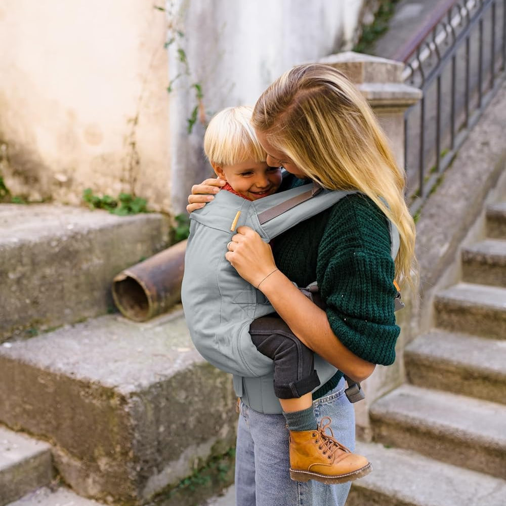 Woman carrying a 3 year old child in a beco Toddlder carrier on stone steps.