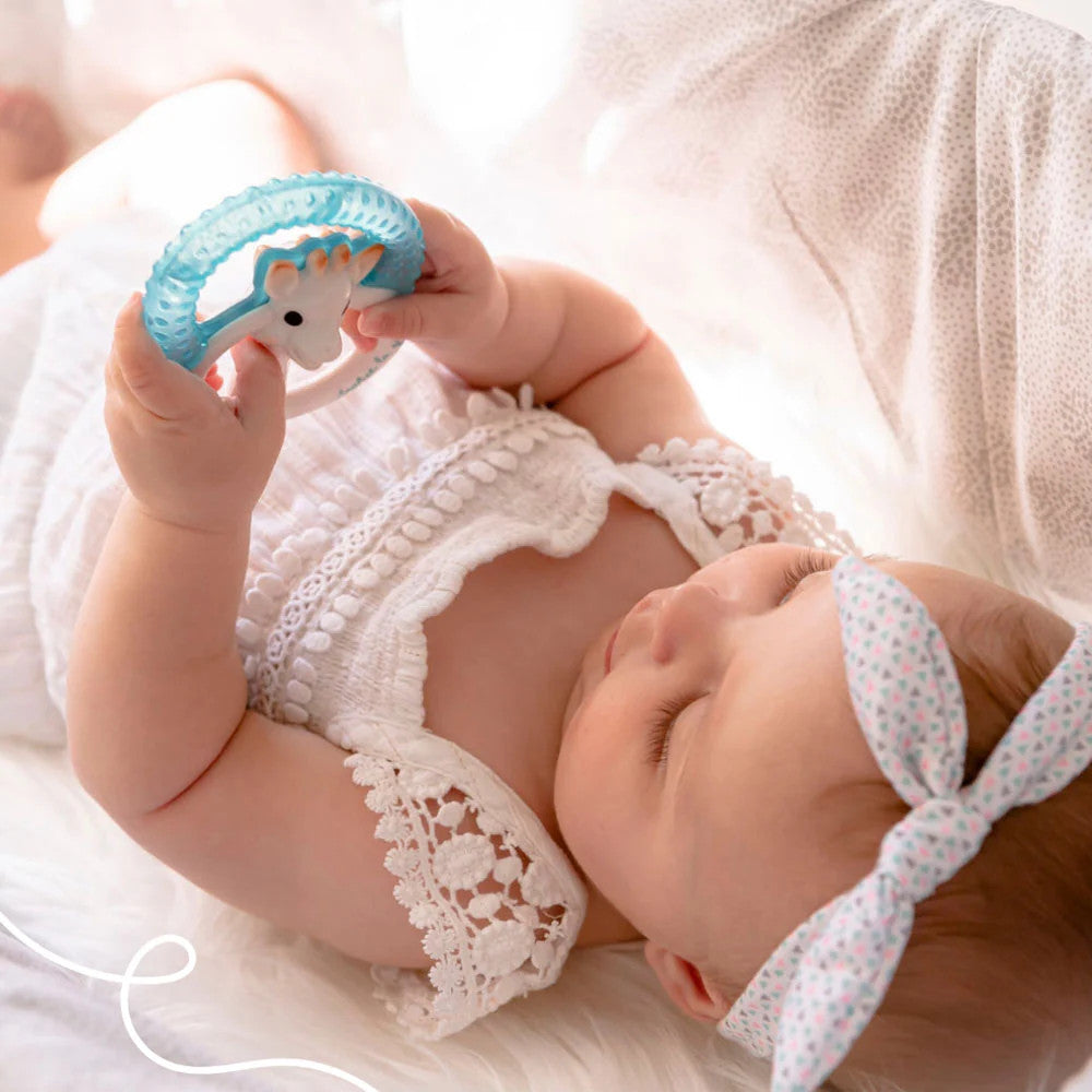 A baby holding a Sophie La Giraffe - Cooling Teething Ring while lying down. 