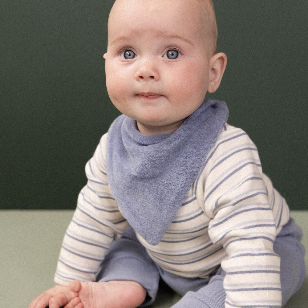 Baby wearing a striped shirt and purple /blue terry cloth bib against a green background