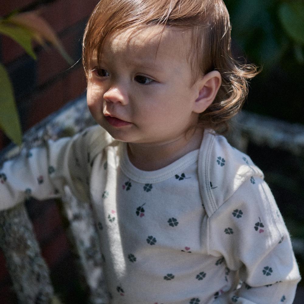 Child wearing a cream coloured bodysuit with clover print in an outdoor setting