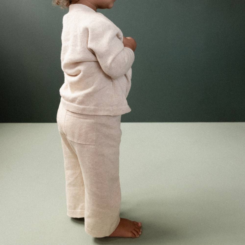Child wearing a beige fine knitted outfit against a plain background