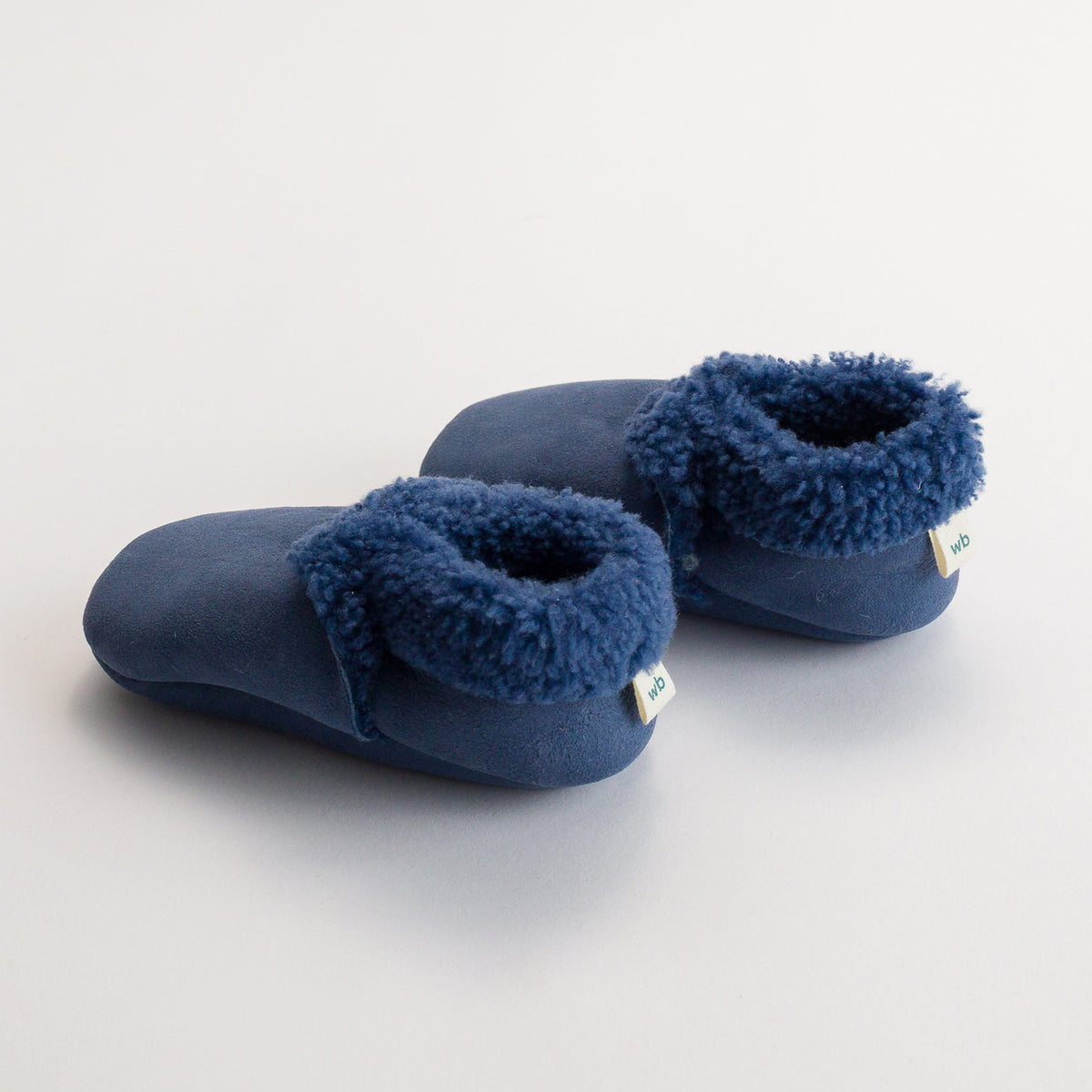 Pair of blue slippers with fuzzy texture with woolbabe tag on a white background
