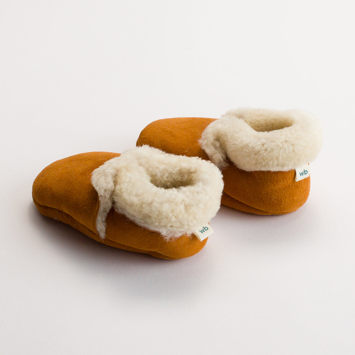 Pair of brown lambskin slippers with white fur lining on a white background