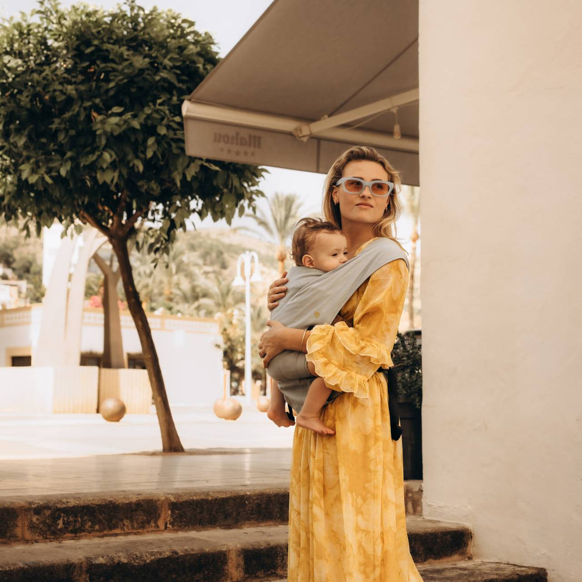 A side shot view of a woman holding her baby in a light blue baby carrier. 