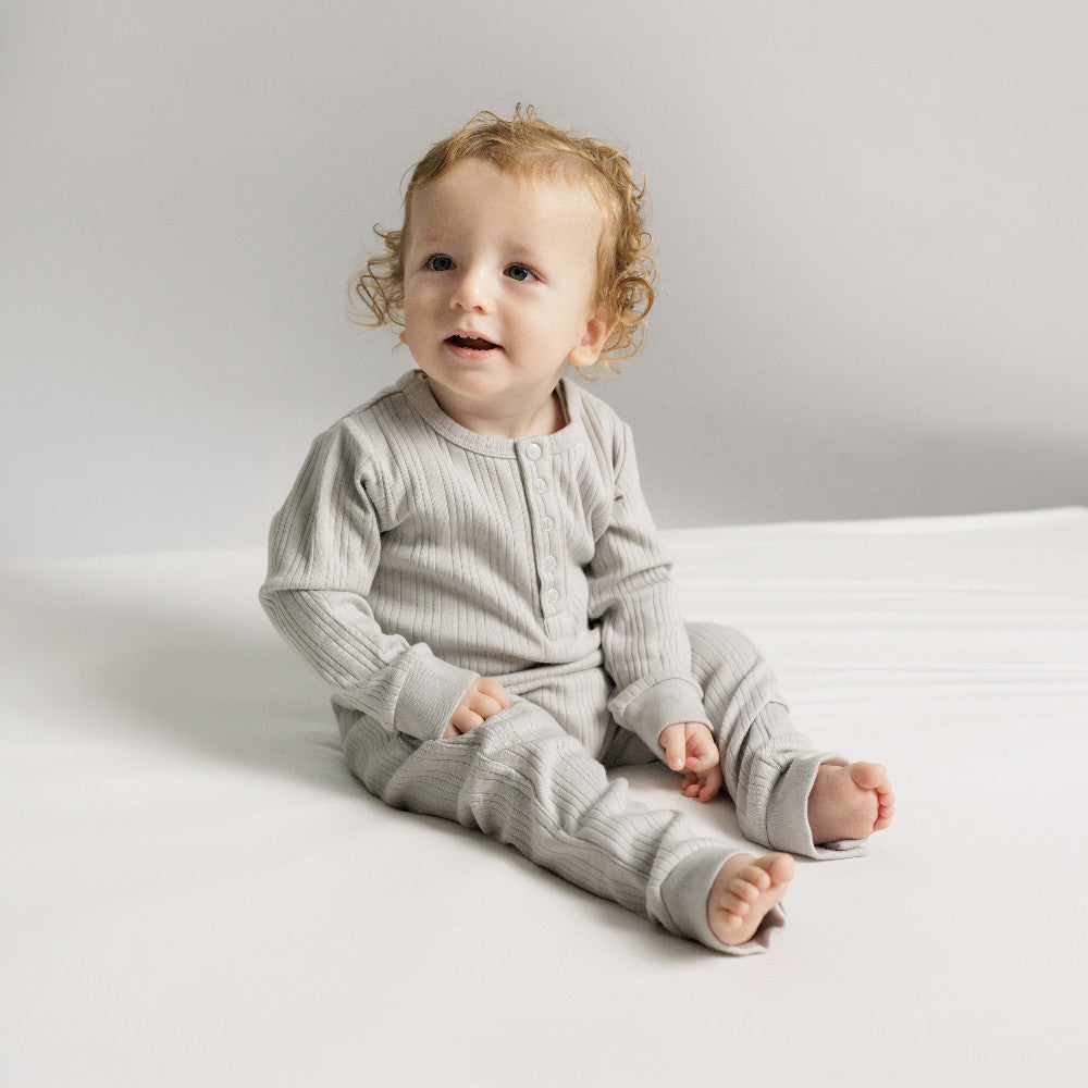 Baby sitting on the floor wearing a pebble mark Woolbabe Merino Cotton Henley Suit. 
