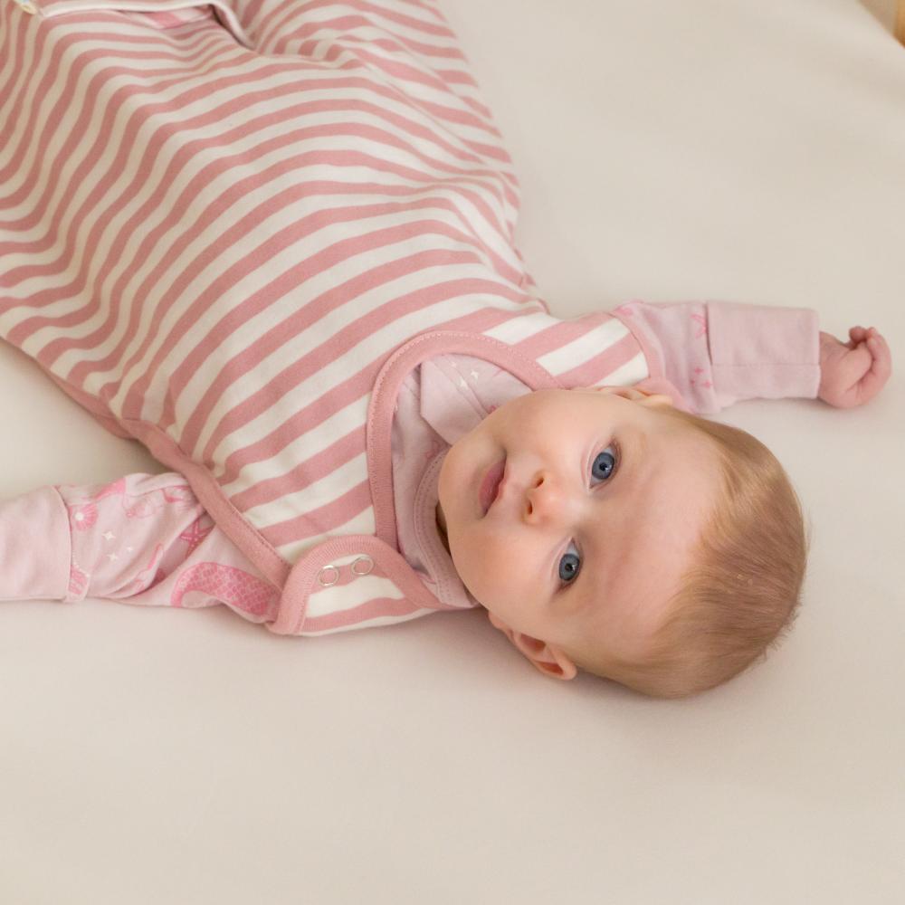Baby wearing a pink and white striped sleeping bag lying on a light surface