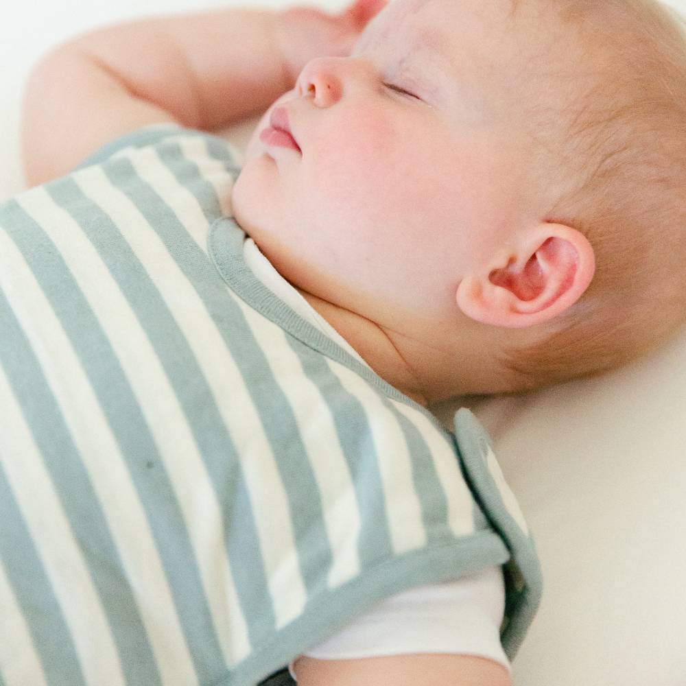 Newborn baby sleeping peacefully wearing a striped woolbabe newborn mini sleeping bag with hands above head