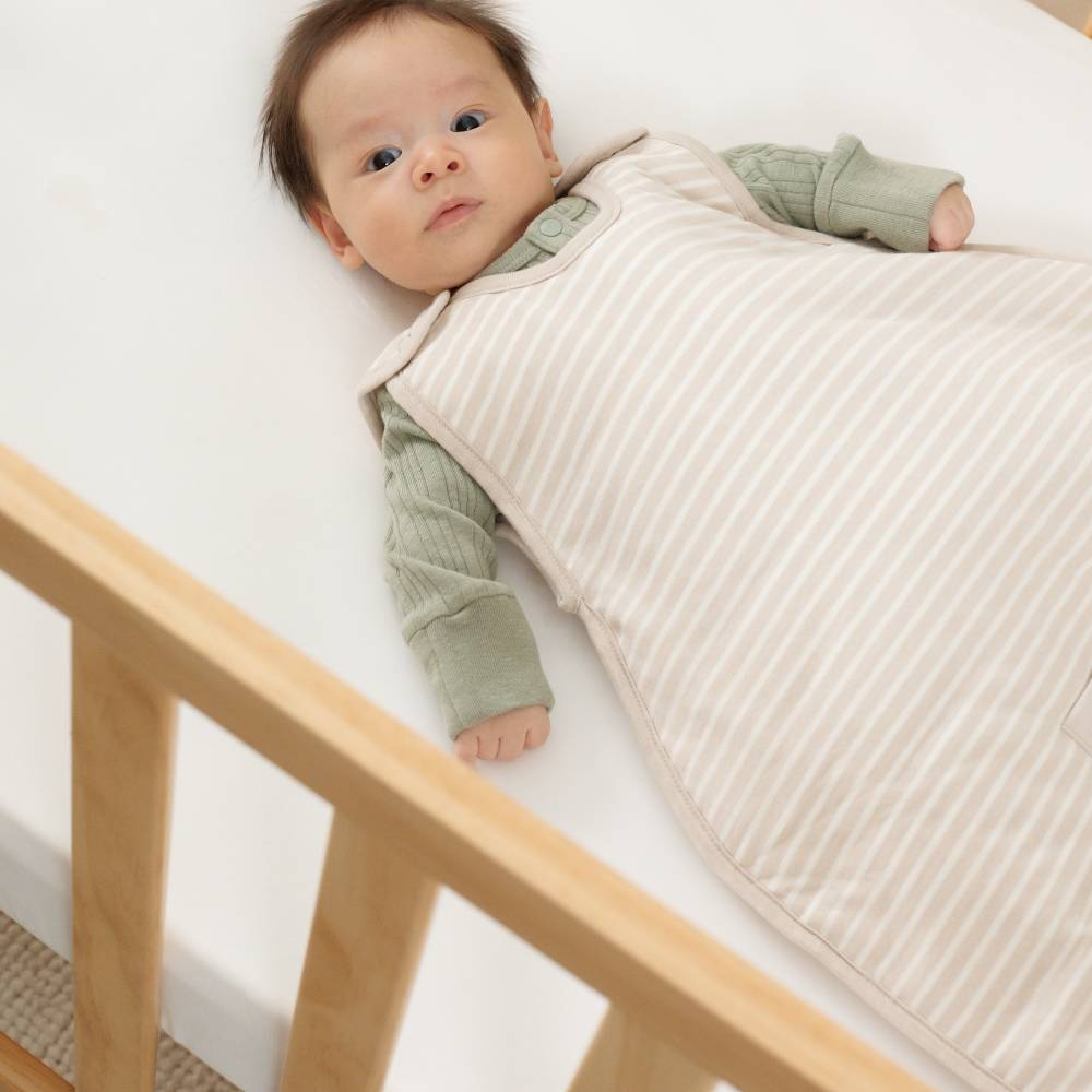 Baby lying in a crib with a beige newborn sleep sack