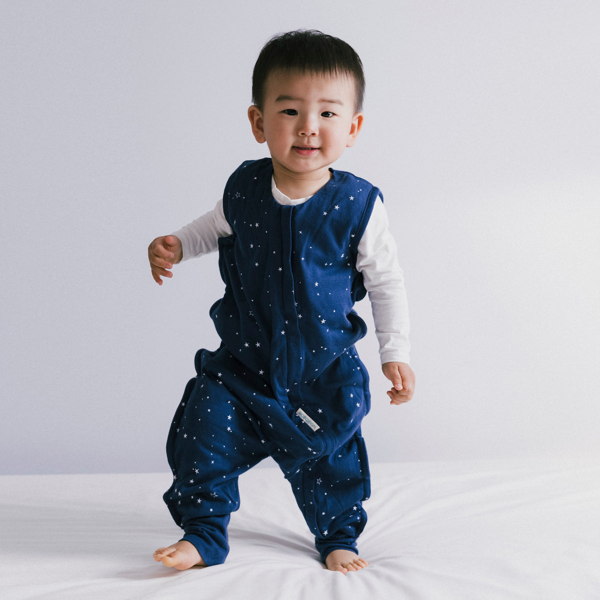 Child wearing a blue star-patterned woolbabe onesie on a white background