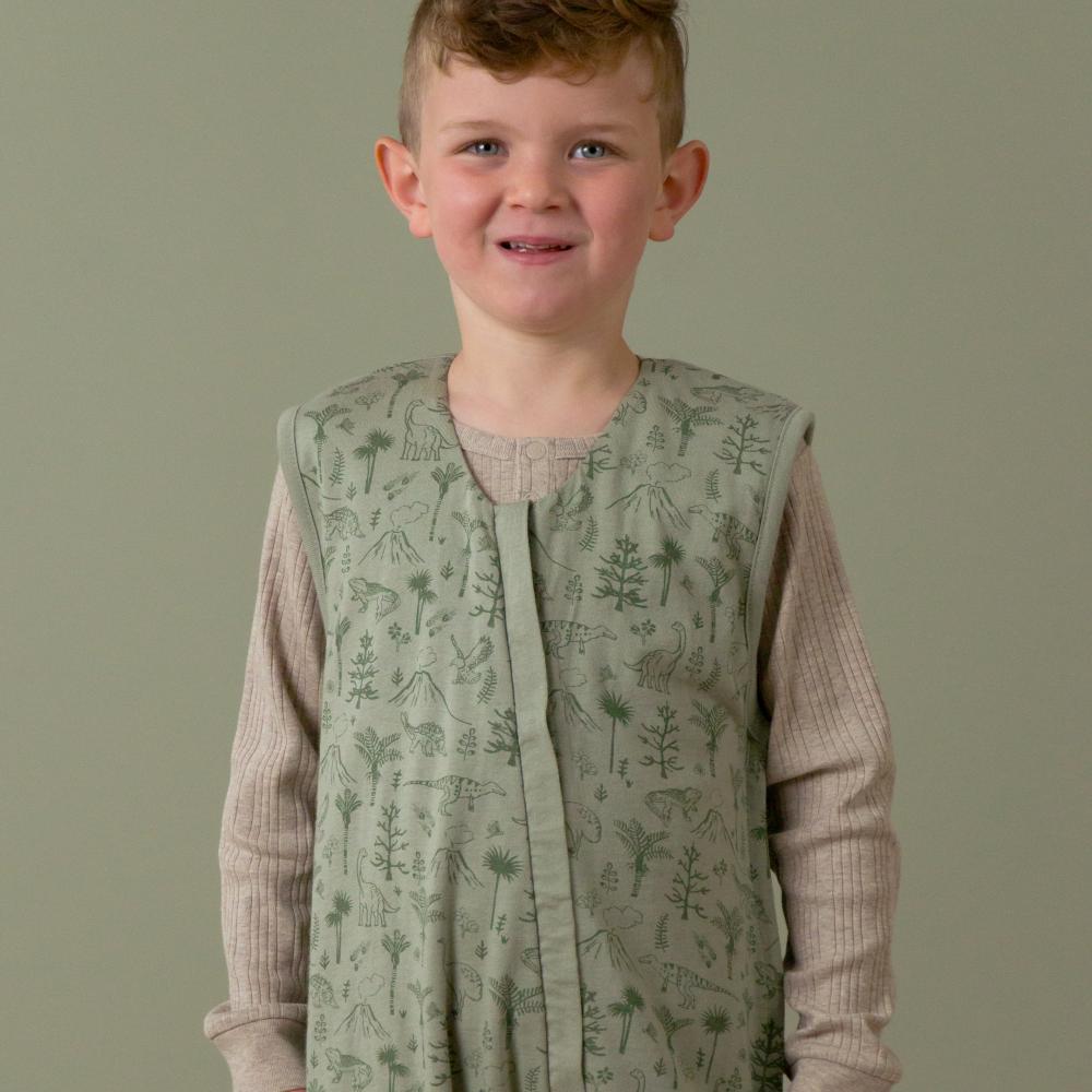 Child wearing a dinosaur print sleepsuit over a long-sleeve shirt against a plain background
