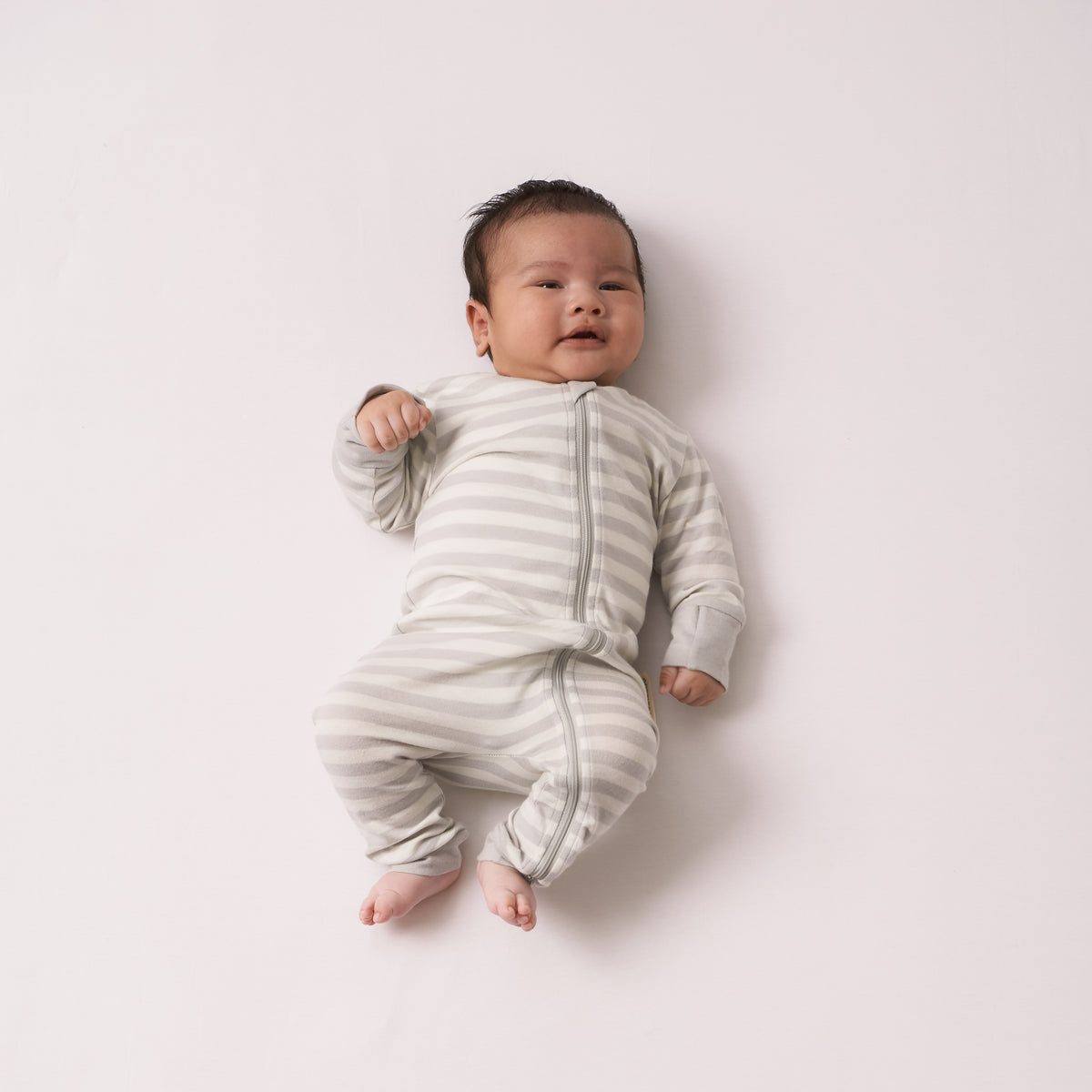 Baby wearing a striped woolbabe onesie on a plain background