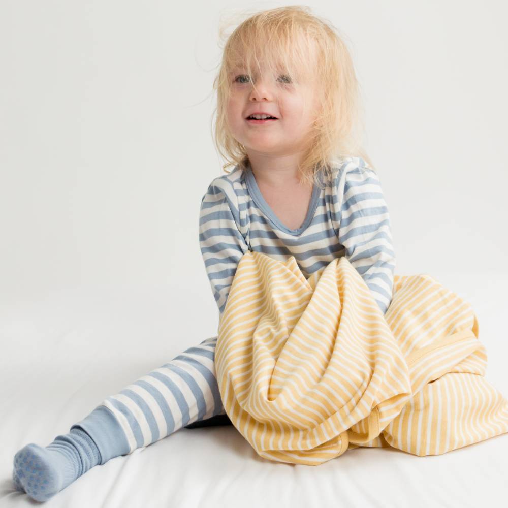 Child wearing striped pajamas with a yellow blanket on a white background