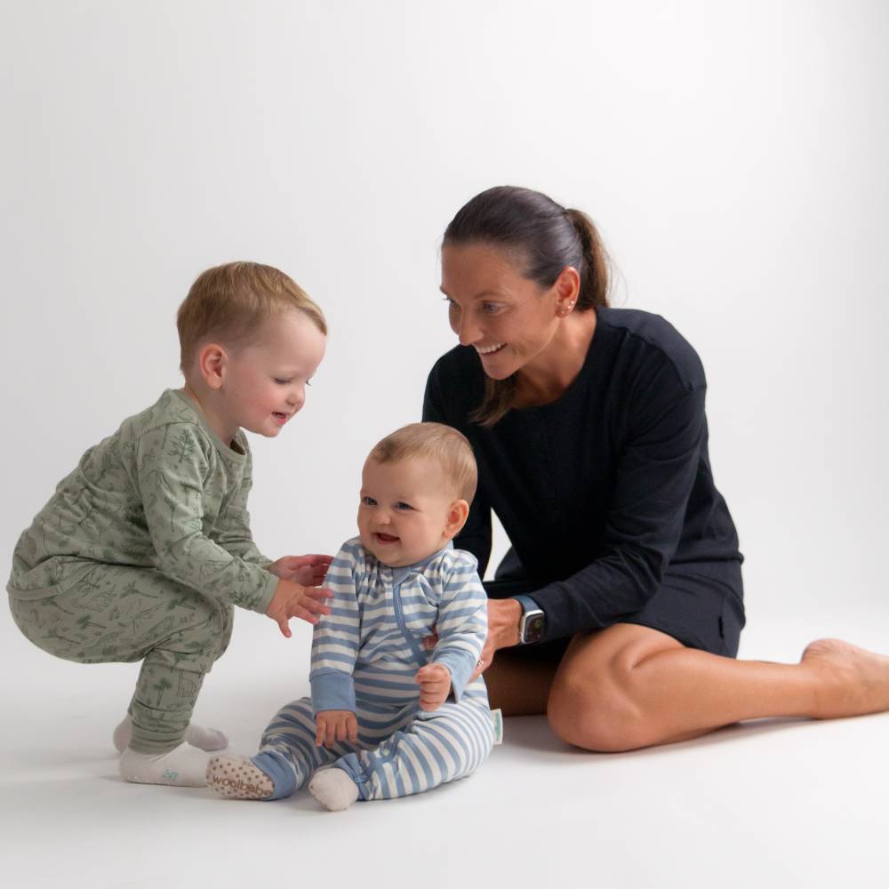Woman sitting on the floor with two children, one of whom is reaching out to touch the other.