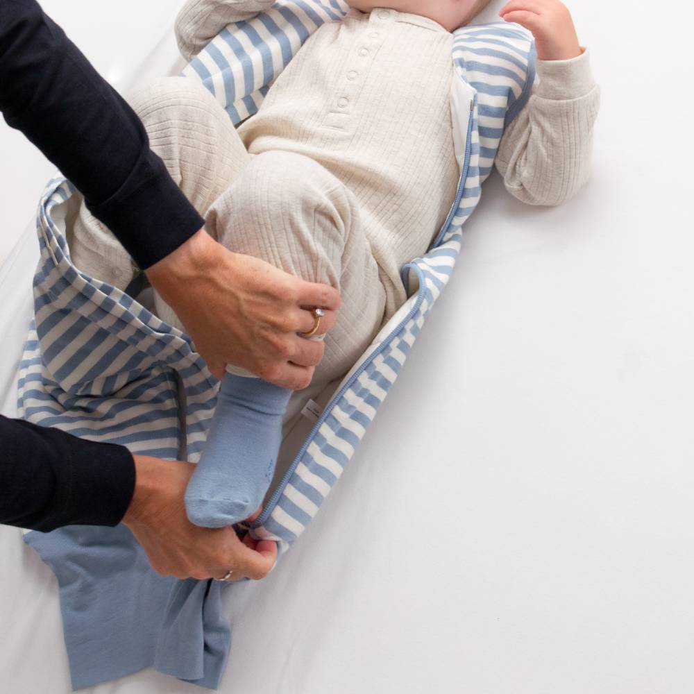 Person holding a baby wrapped in a blue and white striped blanket on a white surface
