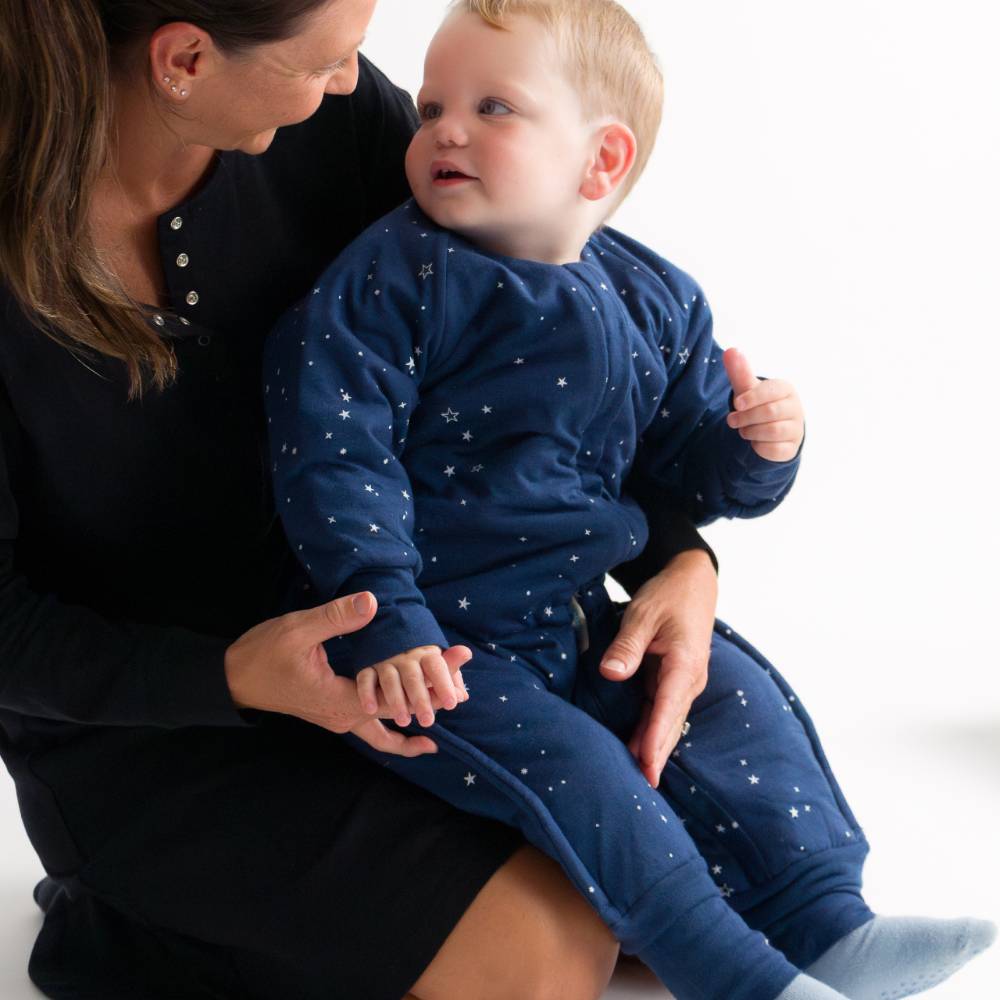 Woman holding a baby wearing a navy blue outfit with star patterns on a white background