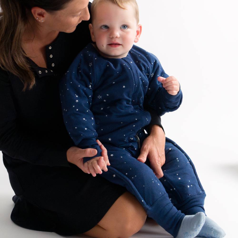 Woman holding a baby wearing matching navy outfits with star patterns on a white background