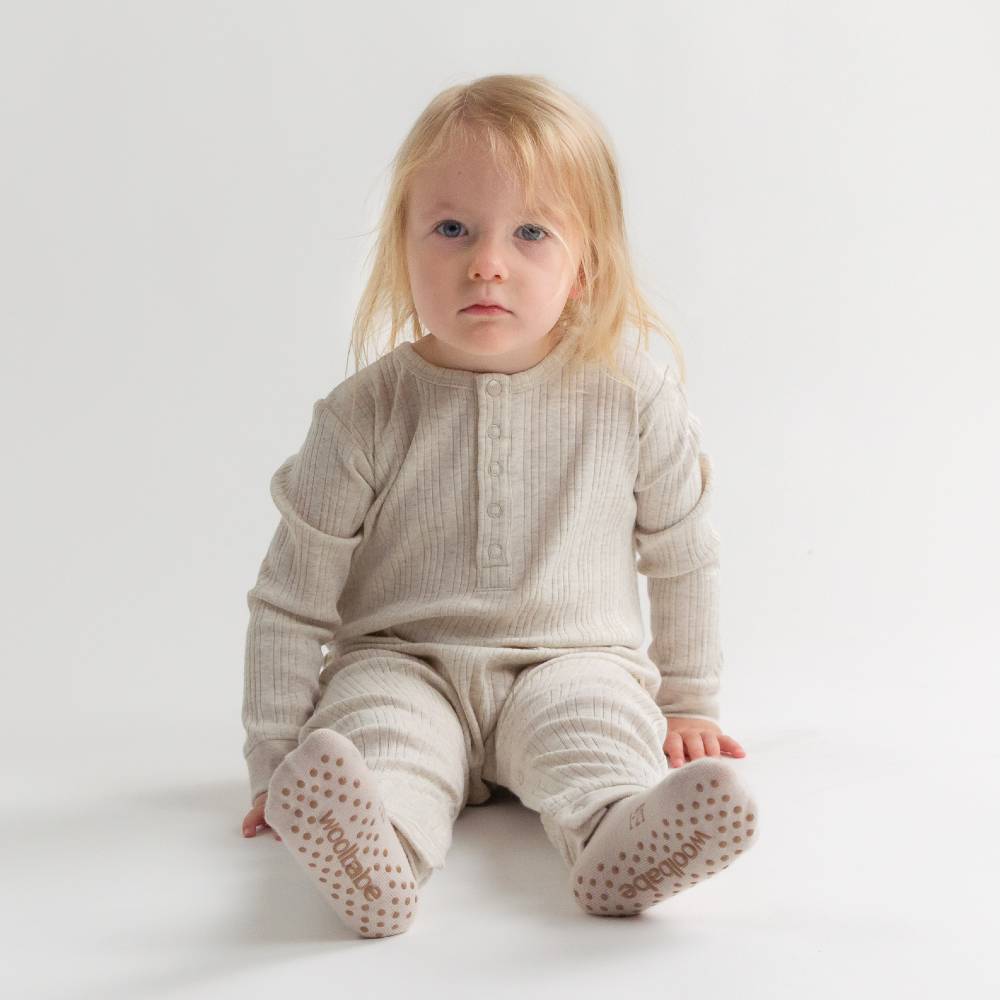 Child wearing a beige outfit with woolbabe sleepy socks on a white background