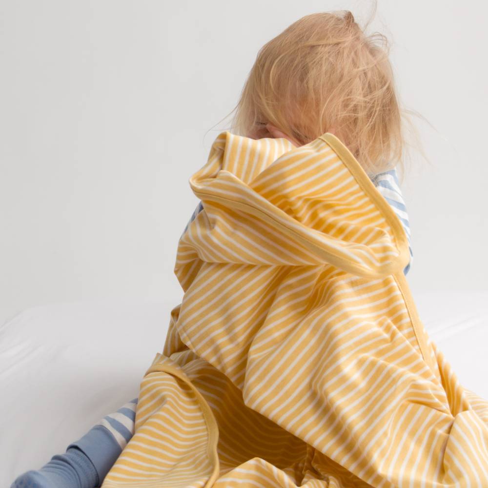 Child wrapped in a yellow and white striped blanket on a white background