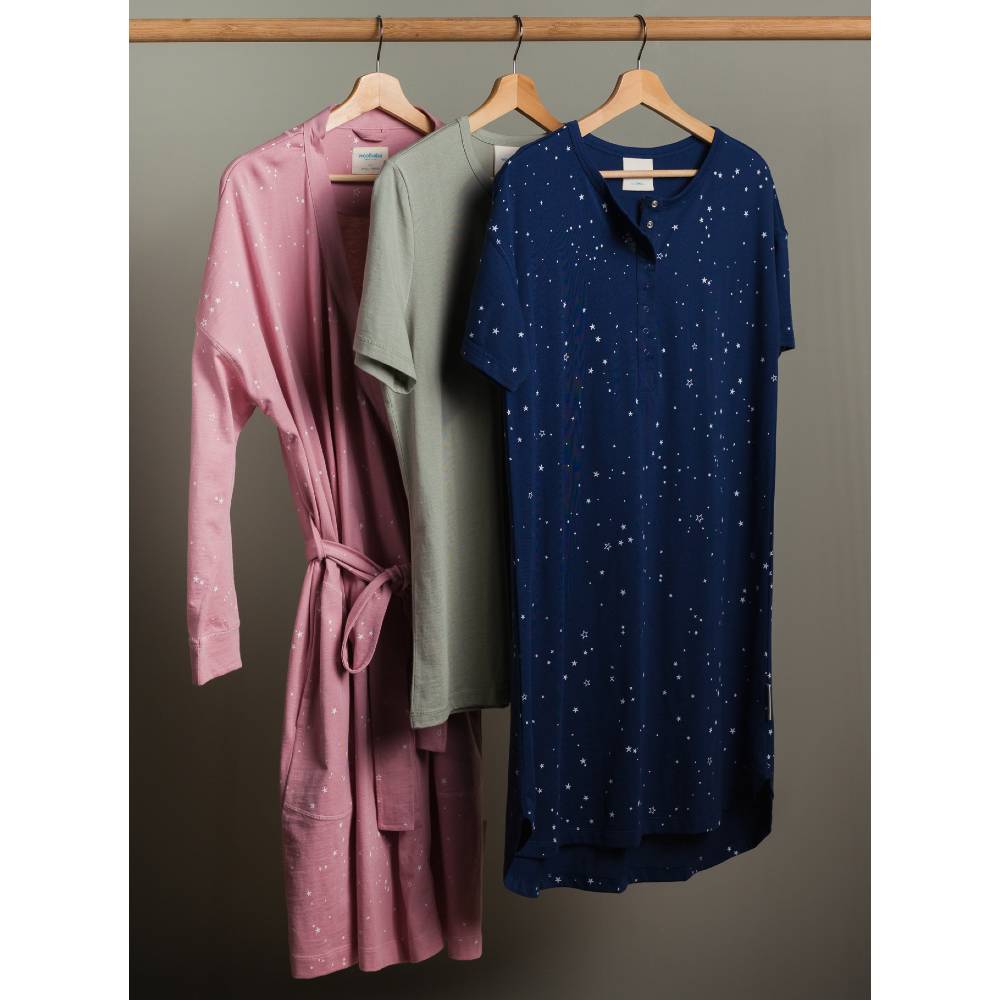 Three dresses in pink, green, and blue hanging on a rack against a gray background