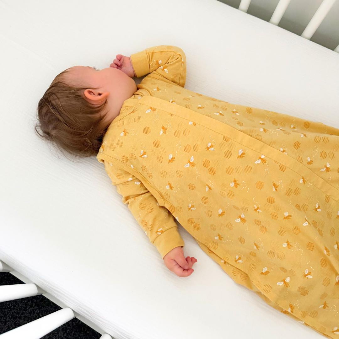 Baby lying in a crib wearing a yellow bee print sleeping bag