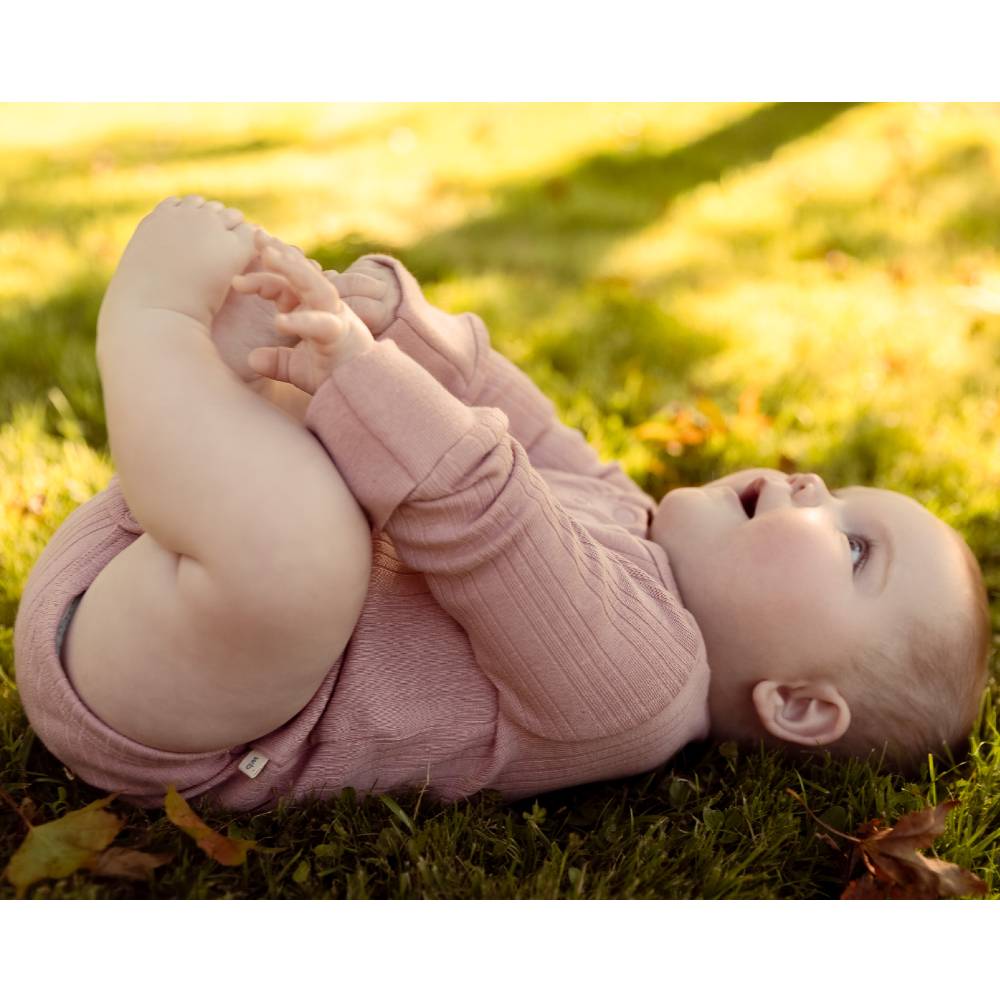 Baby in a pink bodysuit lying on grass with a blurred background