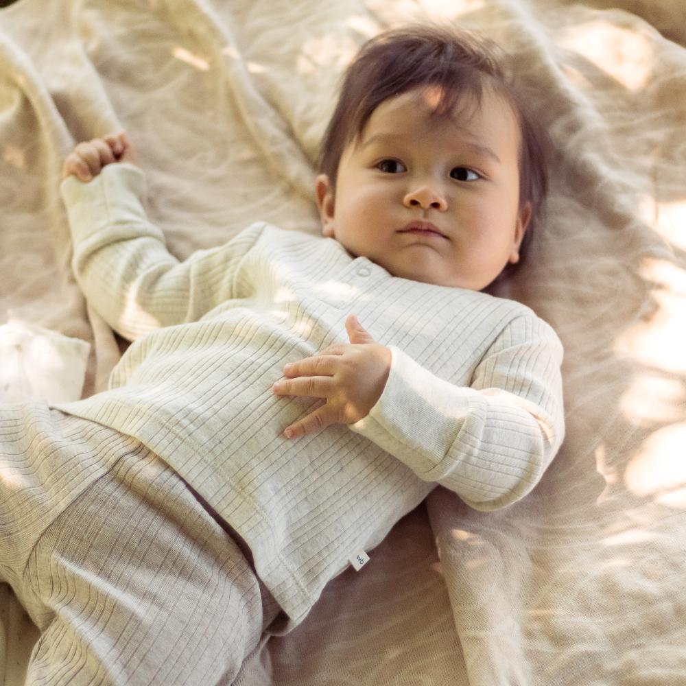 Baby wearing a white outfit lying on a soft, light-colored blanket