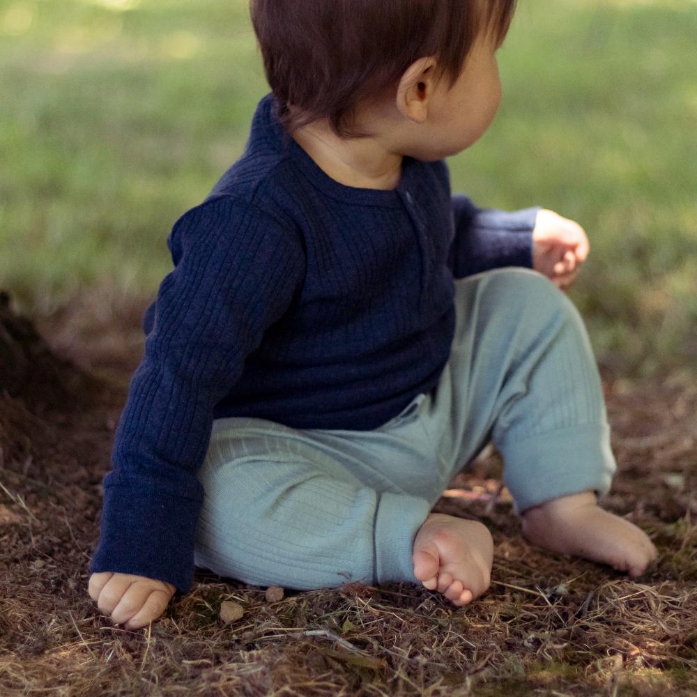 Child sitting on the ground wearing a navy sweater and light blue pants.