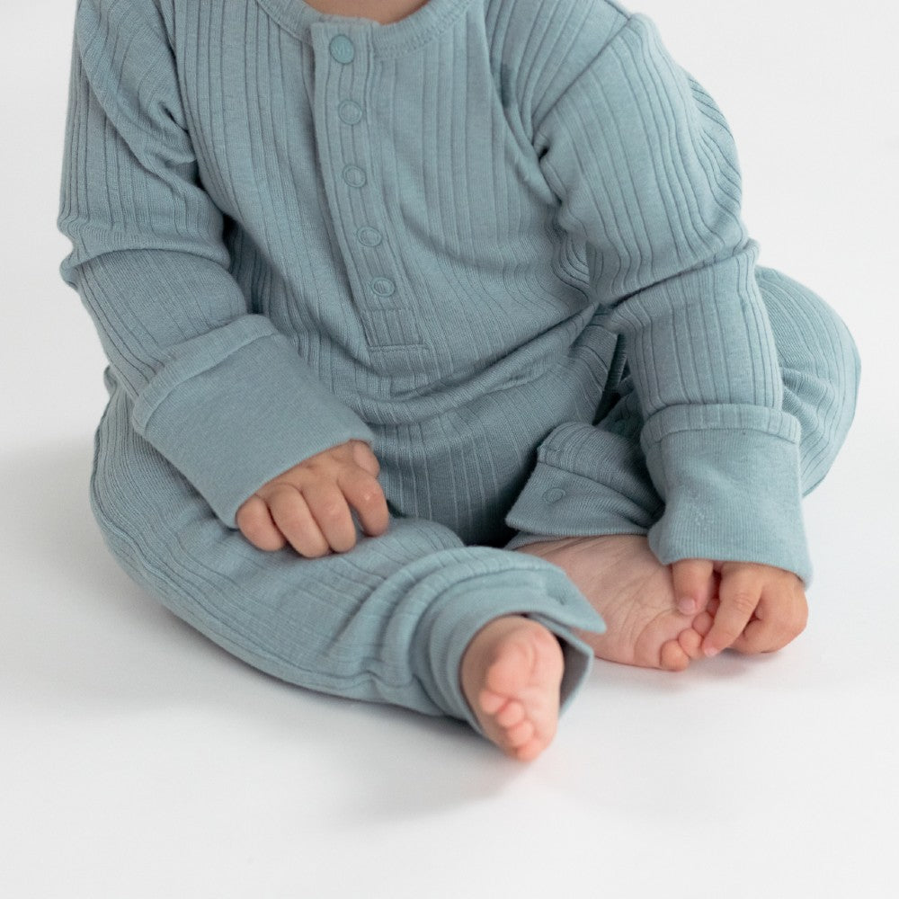 Baby wearing a light blue ribbed outfit on a white background