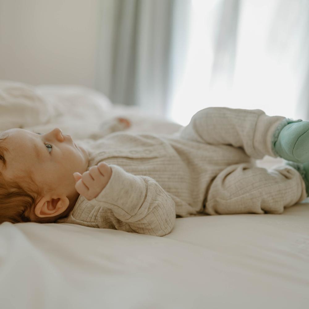 Baby lying on a bed wearing a beige outfit with green socks.