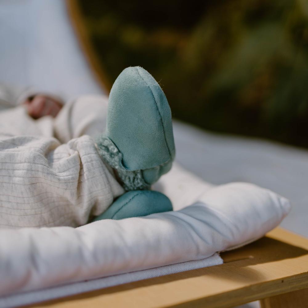Teal wool slippers on a white towel on a wooden surface with a blurred background