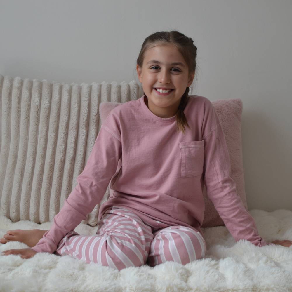 Young girl wearing pink pajamas sitting on a bed with white pillows.