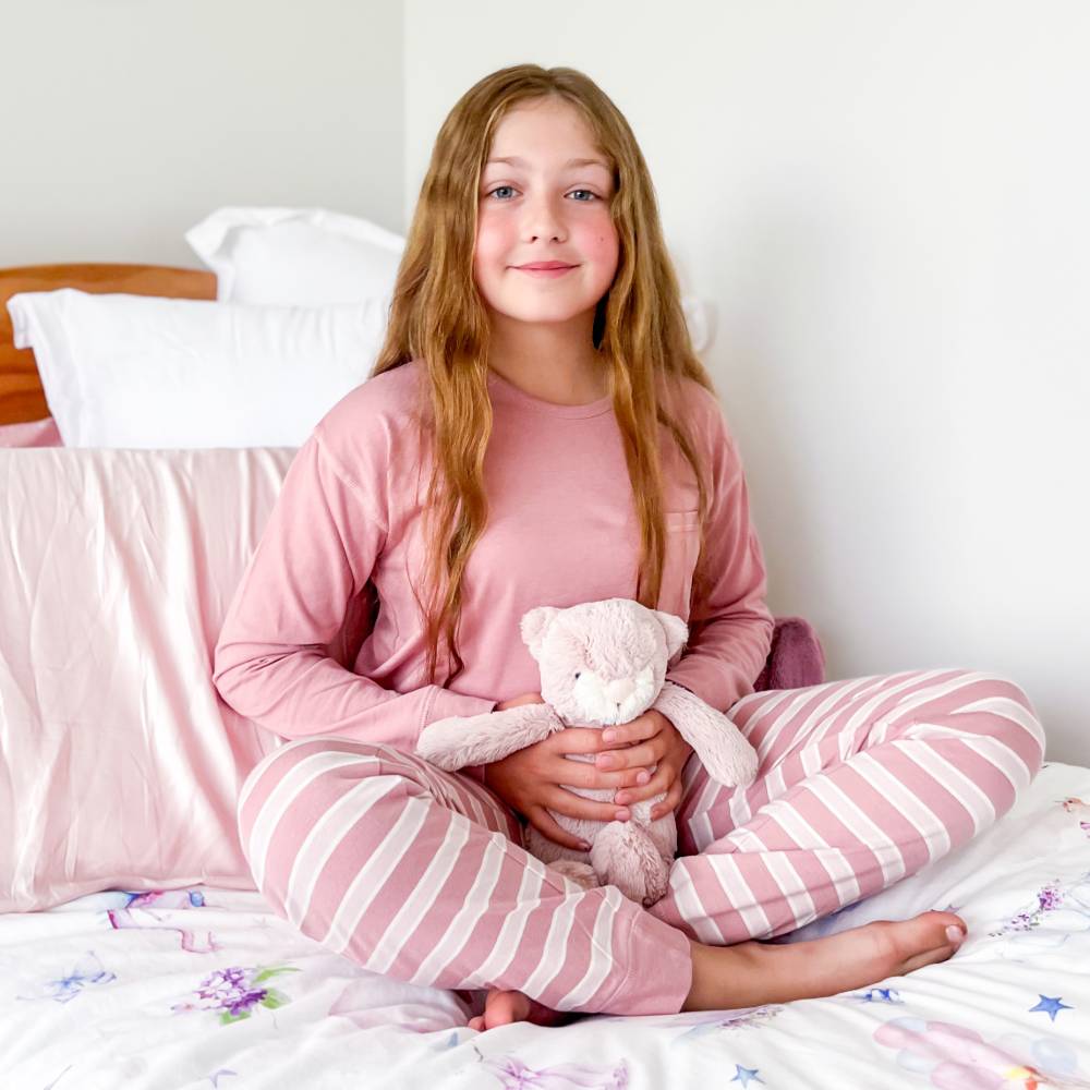 teen girl in pink pajamas holding a teddy bear on a bed.