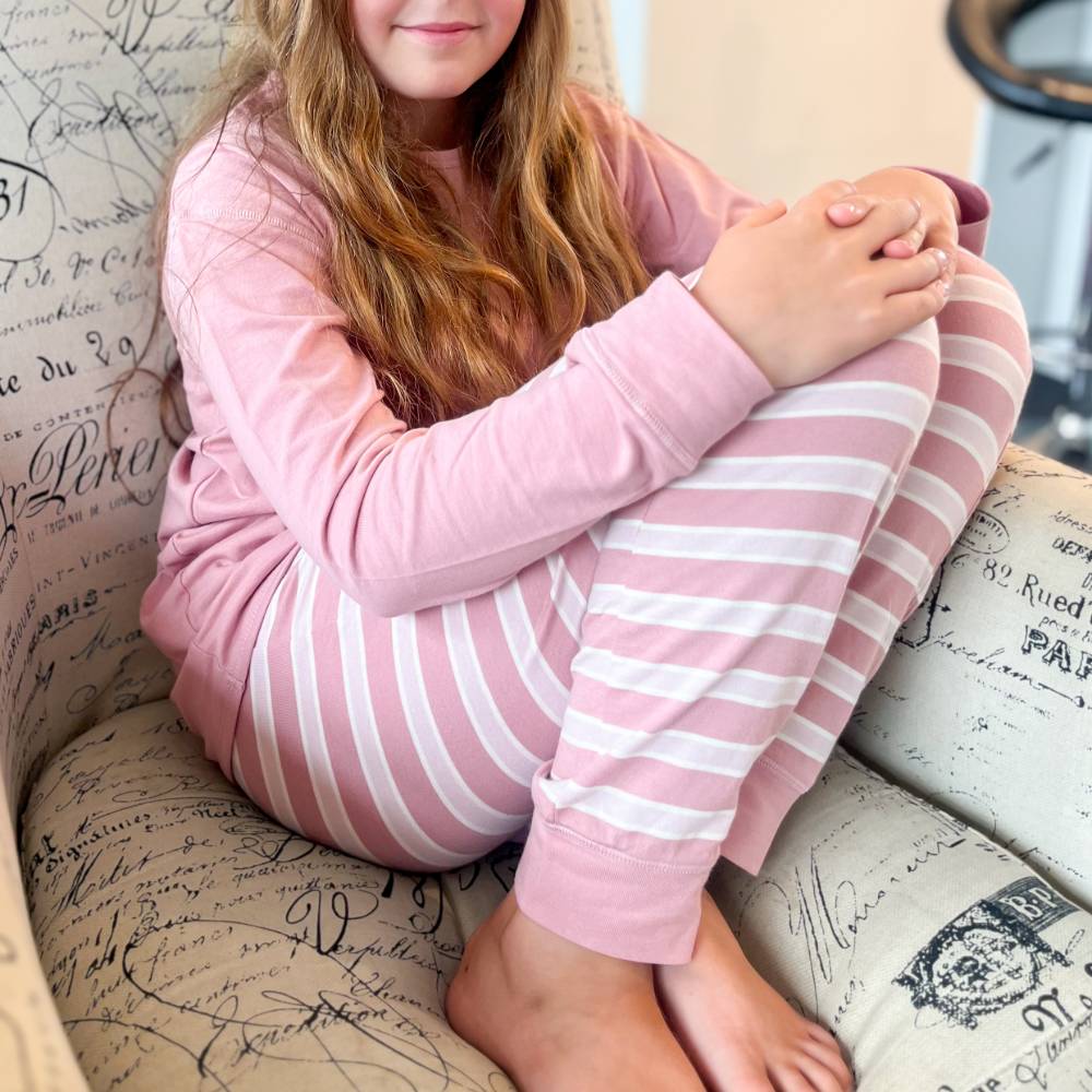 Child wearing pink pajamas with white stripes sitting on a patterned chair.