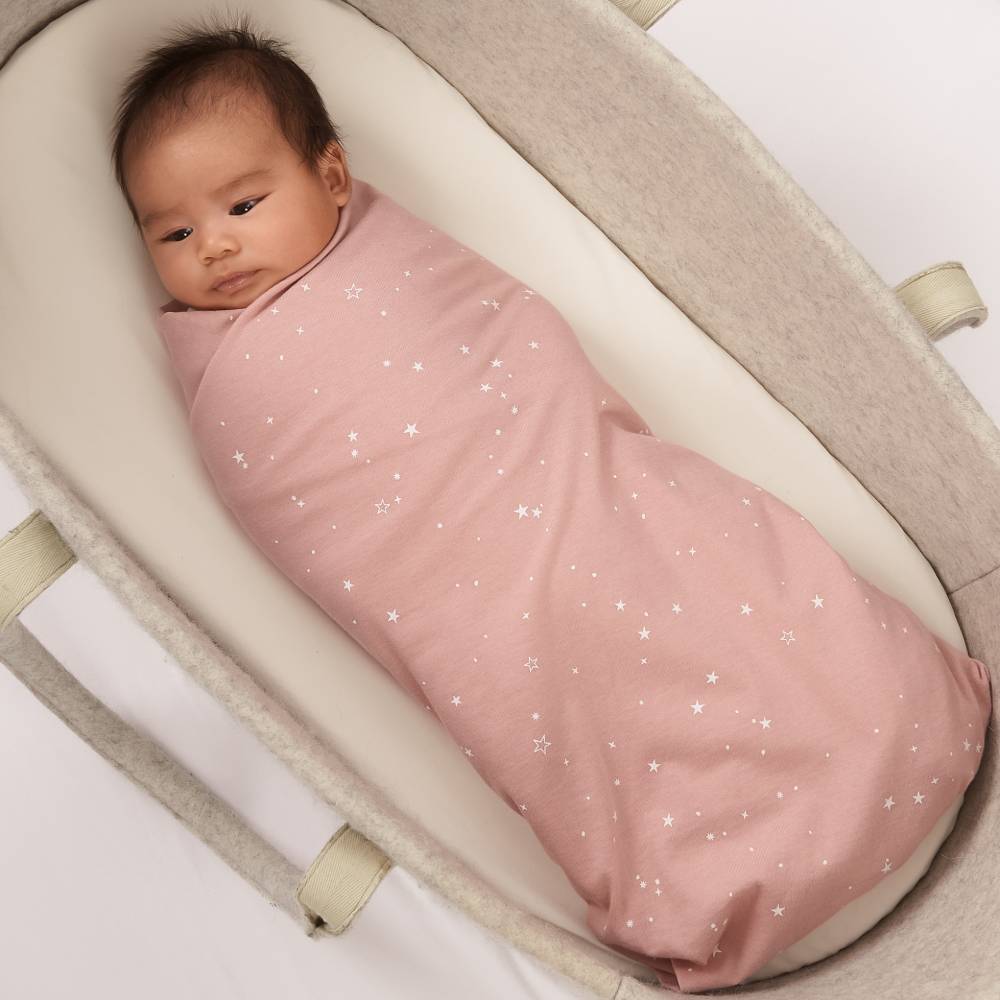 Baby swaddled in a pink blanket with star patterns in a beige crib.