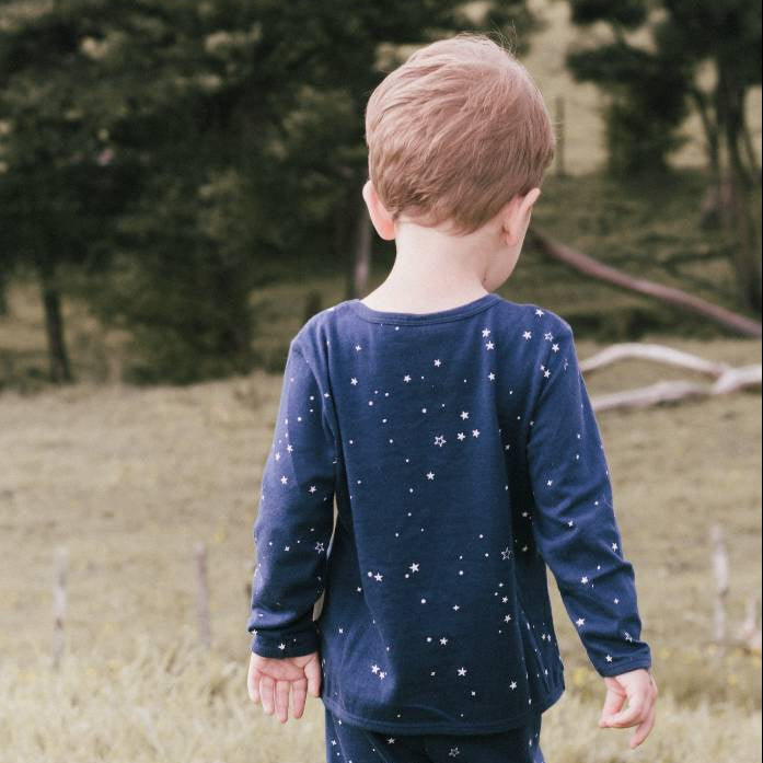 Child wearing a navy blue outfit with star patterns standing in a field with trees in the background