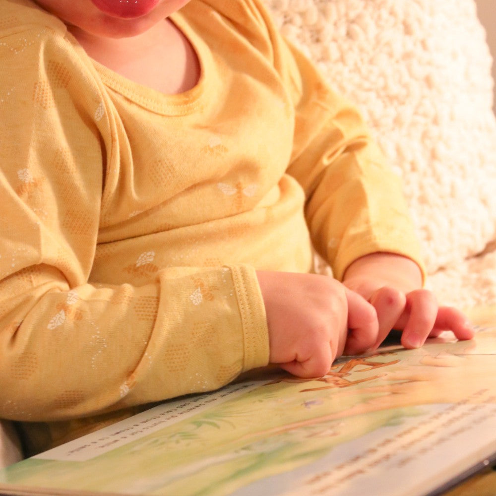 Child in a yellow bee pyjamas holding a book with a soft focus background
