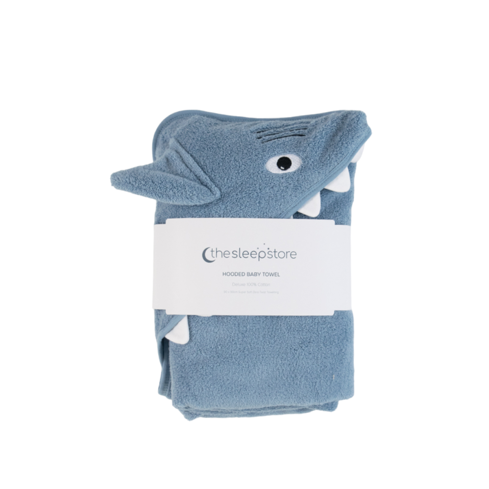 A folded dusty blue hooded terry cotton baby towel shaped like a shark, featuring a white paper label from 'thesleepstore' wrapped around the middle, set against a plain white background.