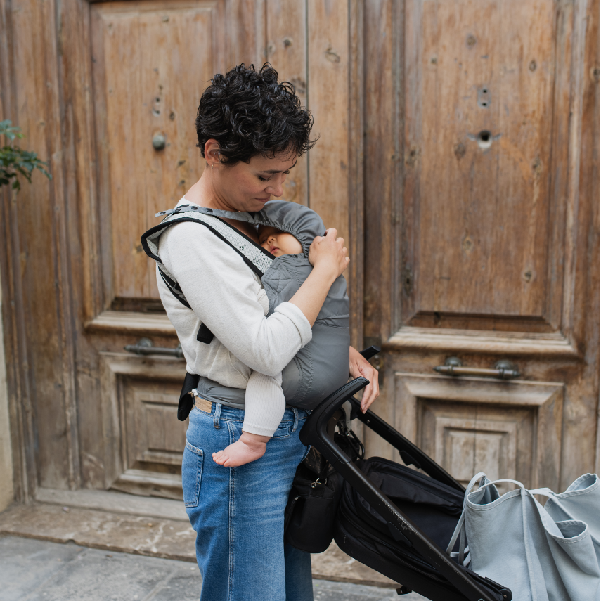 Woman holding a baby in a carrier with a stroller against a wooden door background