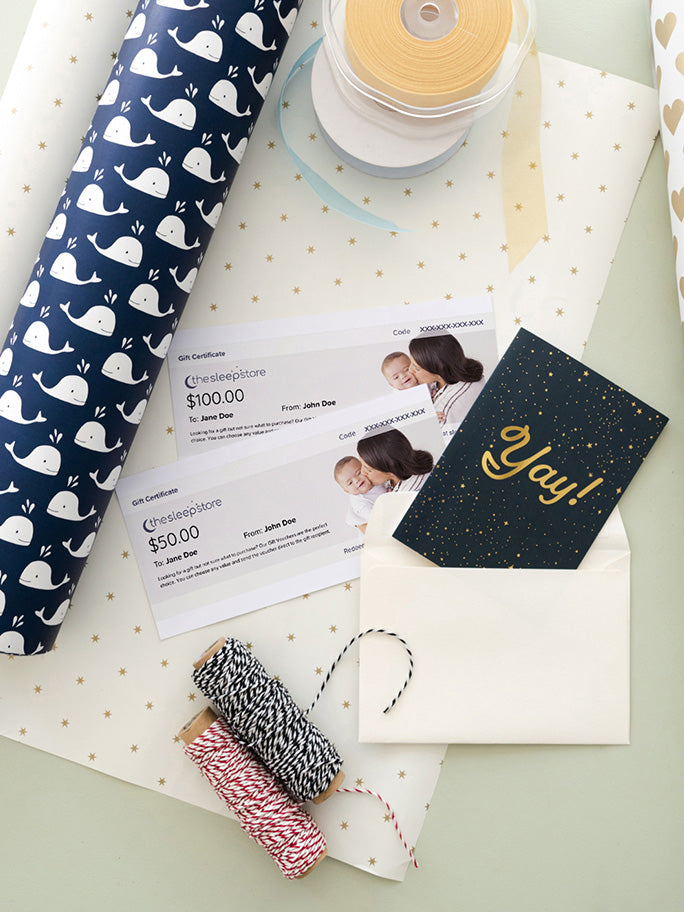 A styled flat-lay of 2 x gift vouchers, gift wrap and gift accessories on a pale green background. 